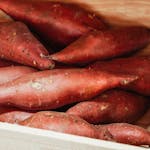 Close-up of fresh sweet potatoes in a wooden crate, ideal for cooking.